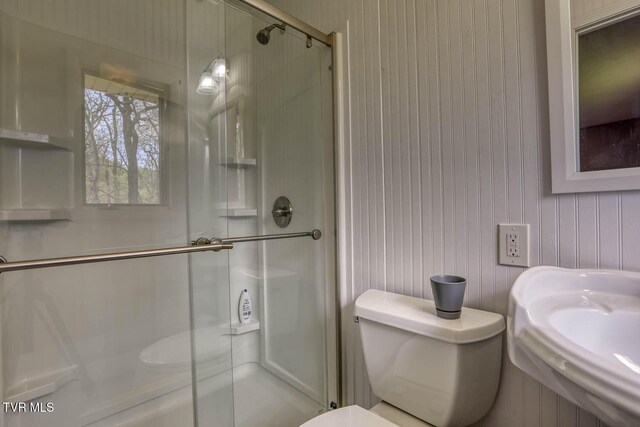 bathroom featuring toilet, wooden walls, and a shower stall