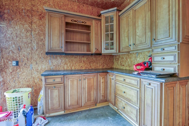 kitchen with brown cabinetry, dark countertops, and glass insert cabinets
