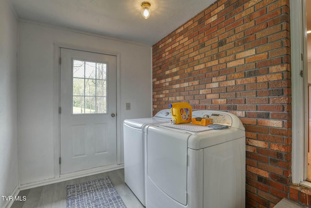 laundry area with wood finished floors, laundry area, brick wall, washer and dryer, and baseboards