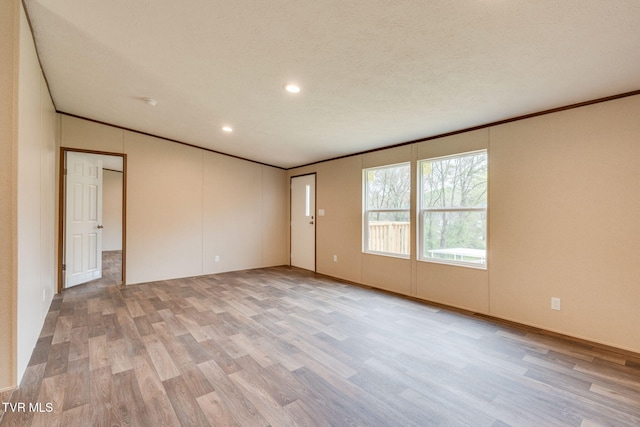empty room with recessed lighting, light wood finished floors, a textured ceiling, and crown molding