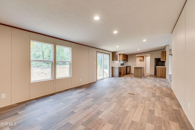 unfurnished living room with light wood-style flooring, a textured ceiling, vaulted ceiling, and recessed lighting