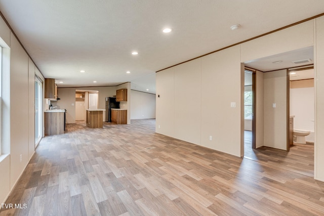 unfurnished living room with light wood finished floors, visible vents, and ornamental molding