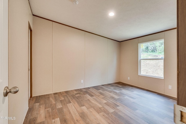 spare room featuring light wood-type flooring, crown molding, and a textured ceiling