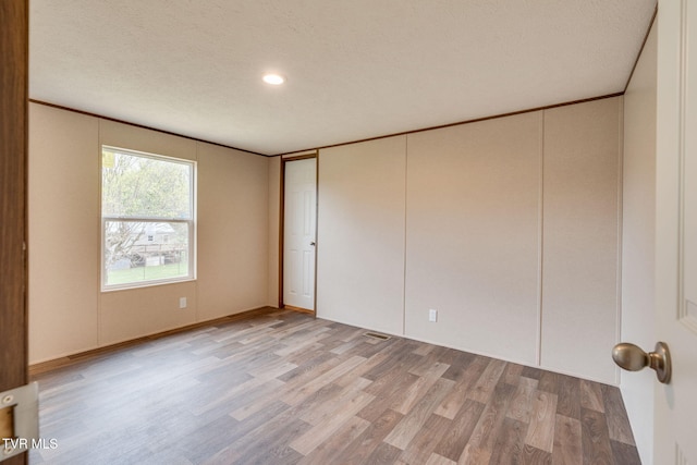 unfurnished bedroom featuring visible vents, light wood-type flooring, a textured ceiling, and ornamental molding