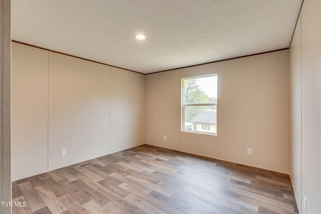 unfurnished room featuring light wood finished floors, a textured ceiling, and crown molding