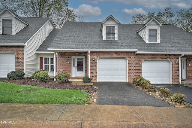 cape cod-style house with a shingled roof, driveway, a garage, and brick siding