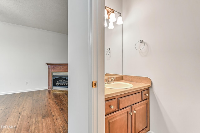 bathroom with crown molding, a fireplace, vanity, wood finished floors, and baseboards