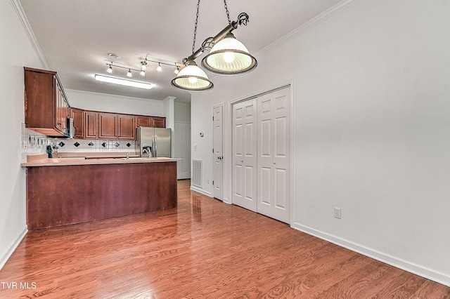 kitchen featuring stainless steel fridge with ice dispenser, a peninsula, light wood-type flooring, ornamental molding, and decorative backsplash