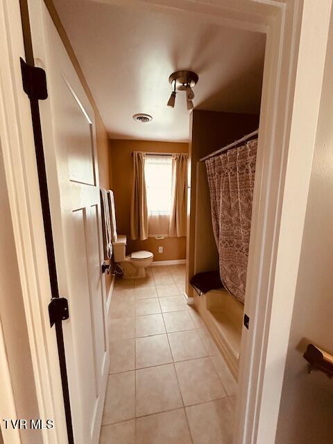 bathroom with toilet, a shower with shower curtain, tile patterned flooring, and visible vents