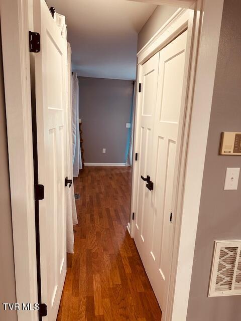 hall featuring visible vents, baseboards, and dark wood-style floors