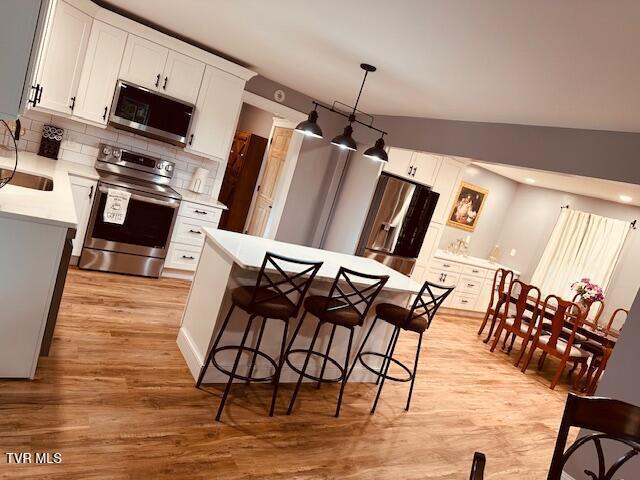 kitchen featuring light wood-type flooring, light countertops, backsplash, white cabinets, and appliances with stainless steel finishes