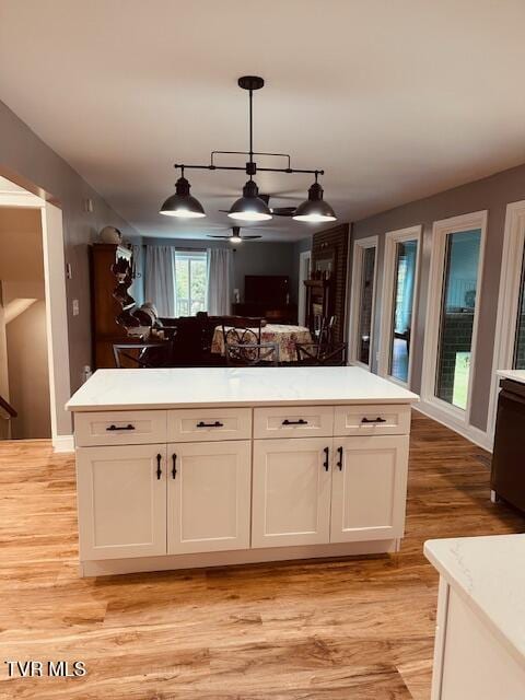 kitchen with light wood-type flooring, a center island, light countertops, white cabinets, and decorative light fixtures