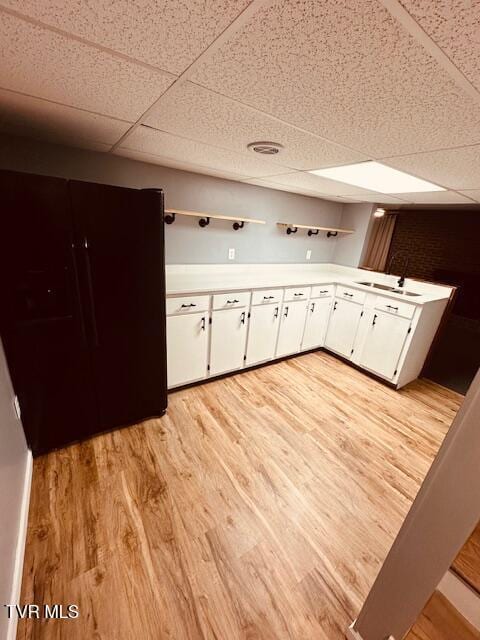 kitchen with a paneled ceiling, light wood-type flooring, a sink, and white cabinetry
