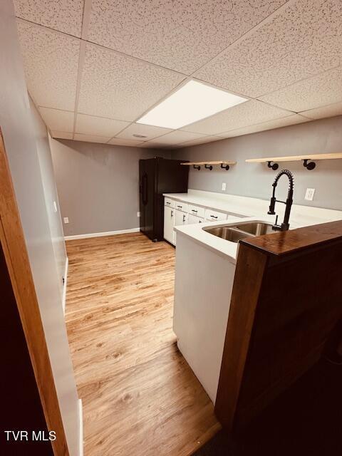 kitchen featuring a sink, light wood-type flooring, a peninsula, white cabinetry, and a drop ceiling