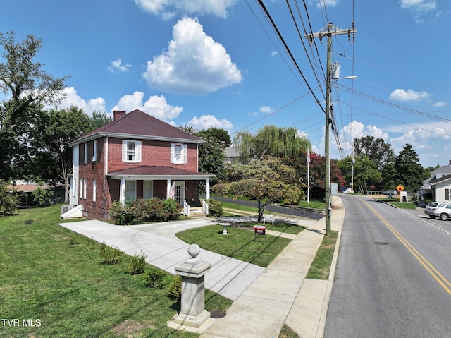 view of front of house with covered porch, brick siding, a chimney, and a front lawn