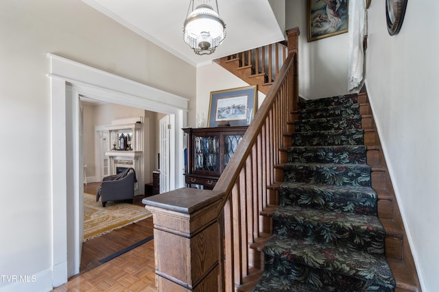 stairway featuring a fireplace, an inviting chandelier, ornamental molding, and baseboards