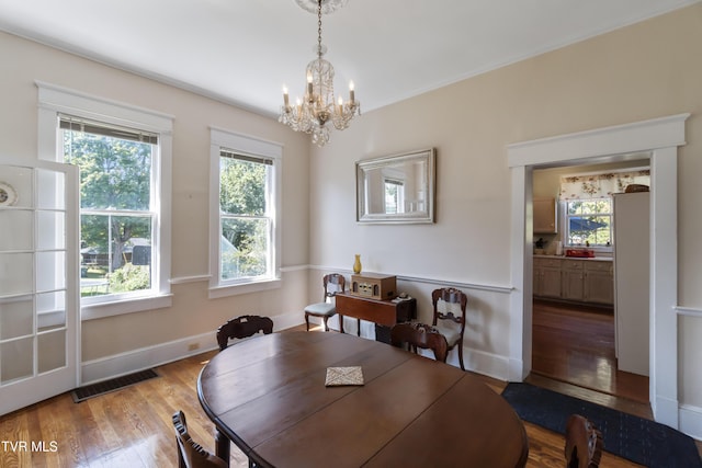 dining space featuring wood finished floors, visible vents, a notable chandelier, and baseboards