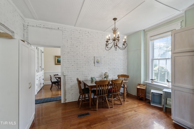 dining space featuring visible vents, wood finished floors, an inviting chandelier, and brick wall