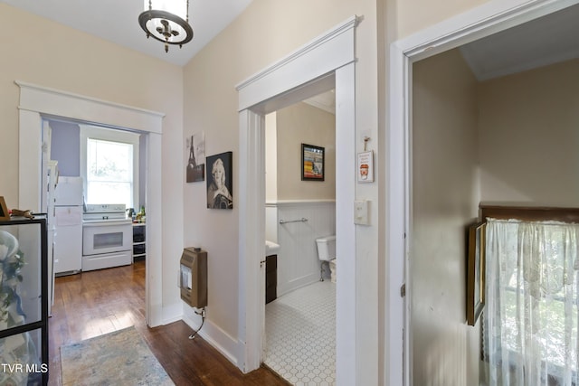 corridor featuring dark wood-type flooring, heating unit, and a wainscoted wall
