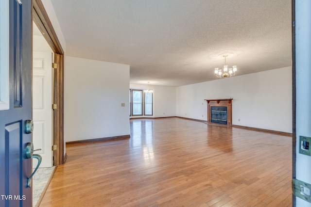 120 Lynnwood Dr, Johnson City, TN 37615 - unfurnished living room with a glass covered fireplace, a notable chandelier, baseboards, light wood-style flooring, and a textured ceiling