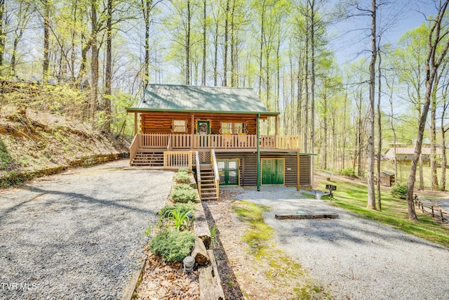 view of front of home featuring log siding, metal roof, stairs, a wooden deck, and gravel driveway
