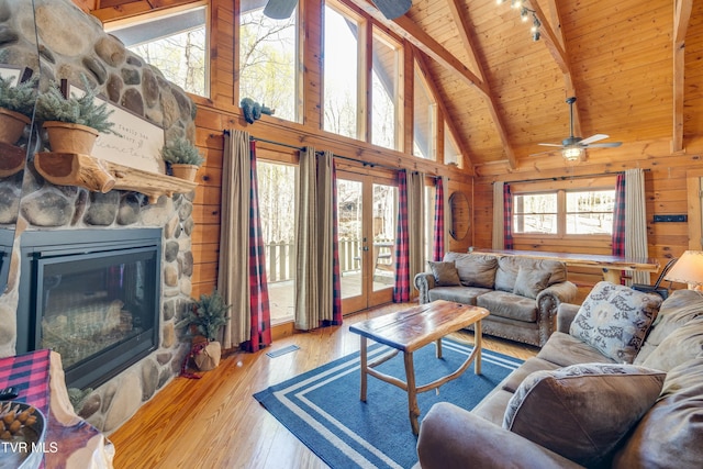living area with ceiling fan, wood ceiling, wooden walls, beamed ceiling, and wood-type flooring