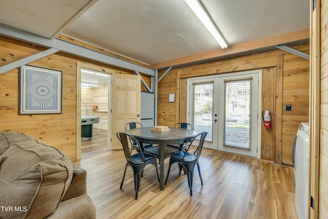 dining area featuring washer and dryer, light wood-style floors, french doors, and wood walls