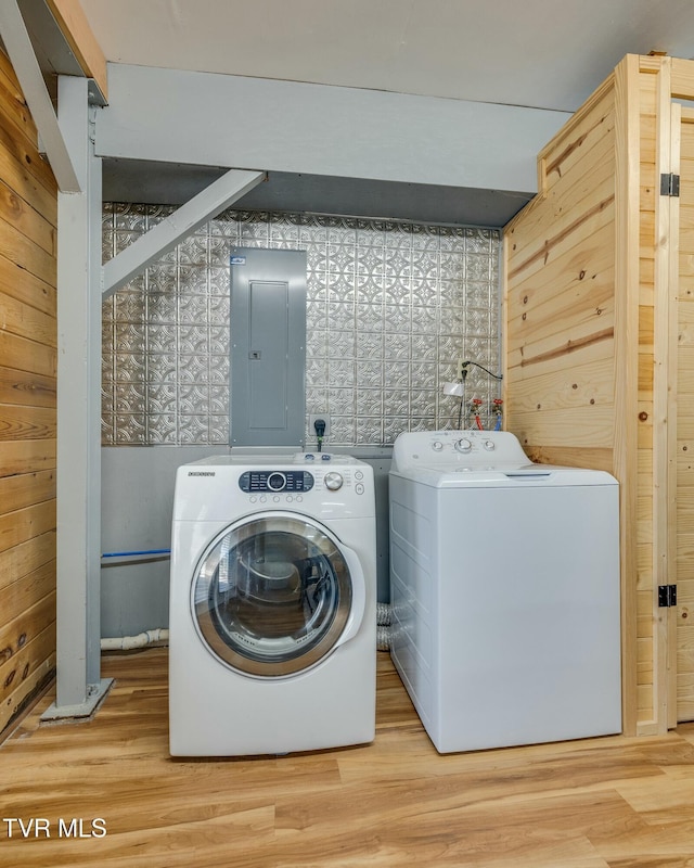 washroom with wood finished floors, wood walls, electric panel, and washing machine and dryer