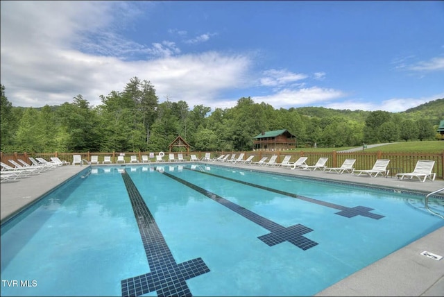 community pool featuring a patio, a wooded view, and fence