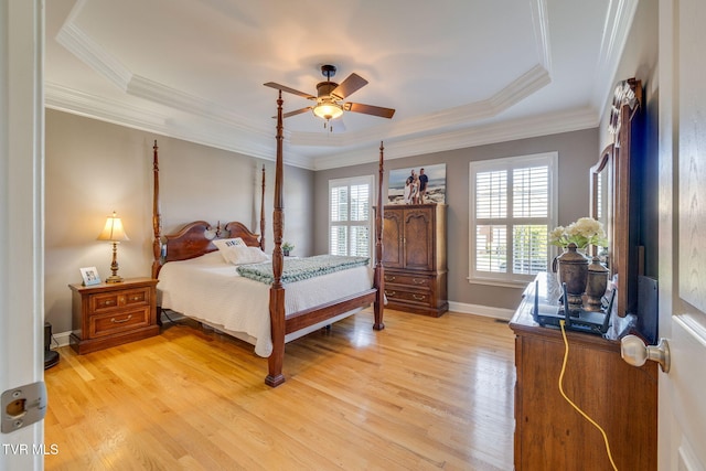 bedroom featuring baseboards, light wood-type flooring, ornamental molding, a ceiling fan, and a tray ceiling