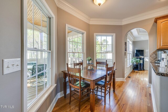 dining room featuring crown molding, baseboards, light wood finished floors, and arched walkways