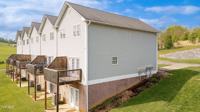 view of side of home featuring brick siding, cooling unit, and a lawn