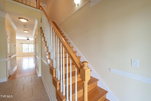 stairway featuring stone tile flooring, baseboards, ornamental molding, and a ceiling fan