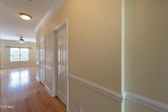 hallway with crown molding, wood finished floors, a textured wall, and baseboards
