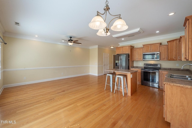 kitchen featuring ceiling fan with notable chandelier, a kitchen bar, a center island, a sink, and stainless steel appliances