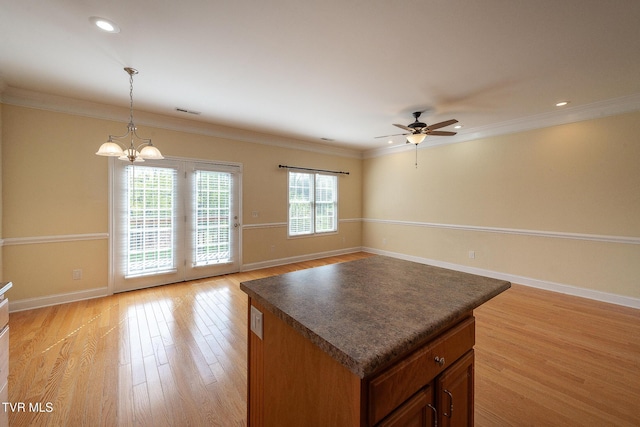 kitchen with light wood-type flooring, ornamental molding, ceiling fan with notable chandelier, and dark countertops