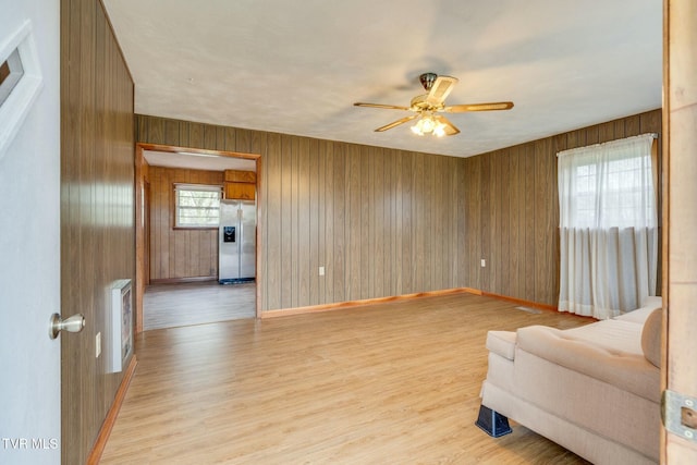 living area with wood walls, light wood-style flooring, baseboards, and a ceiling fan