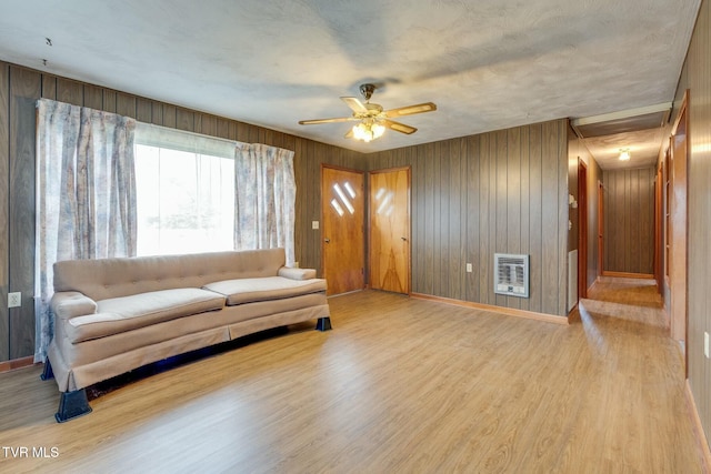 living area with baseboards, a ceiling fan, heating unit, and wood finished floors