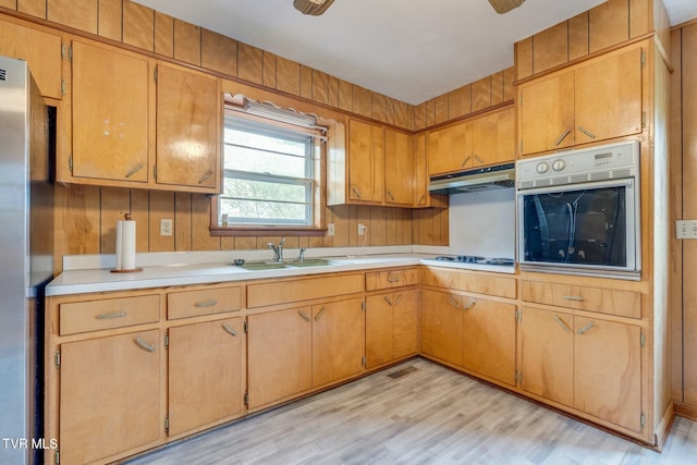 kitchen featuring a sink, light countertops, under cabinet range hood, light wood finished floors, and stainless steel appliances
