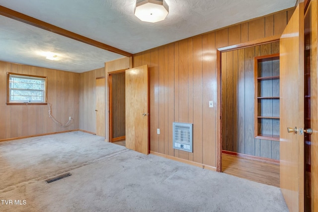 empty room with visible vents, baseboards, heating unit, carpet, and wooden walls