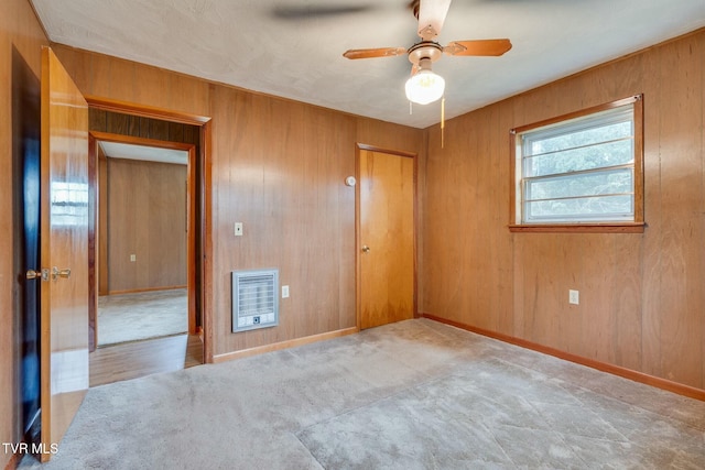 carpeted empty room with wooden walls, ceiling fan, heating unit, and baseboards