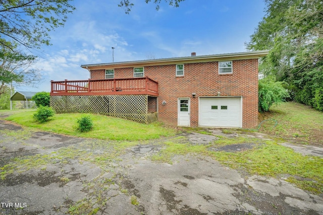 rear view of property with a lawn, a garage, aphalt driveway, brick siding, and a wooden deck