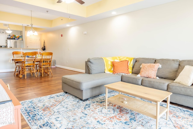 living area featuring baseboards, wood finished floors, ceiling fan, recessed lighting, and a raised ceiling