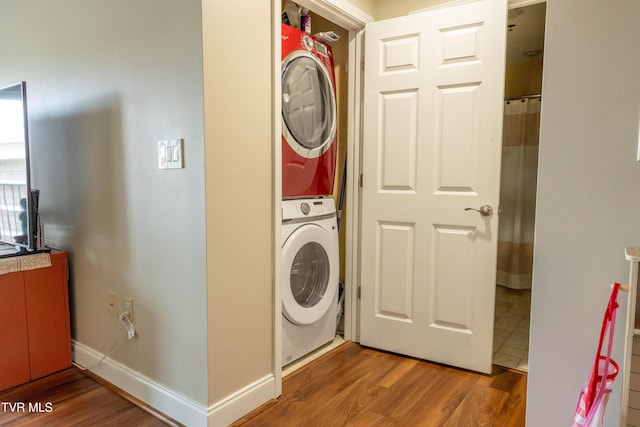 clothes washing area featuring estacked washer and dryer, wood finished floors, and baseboards