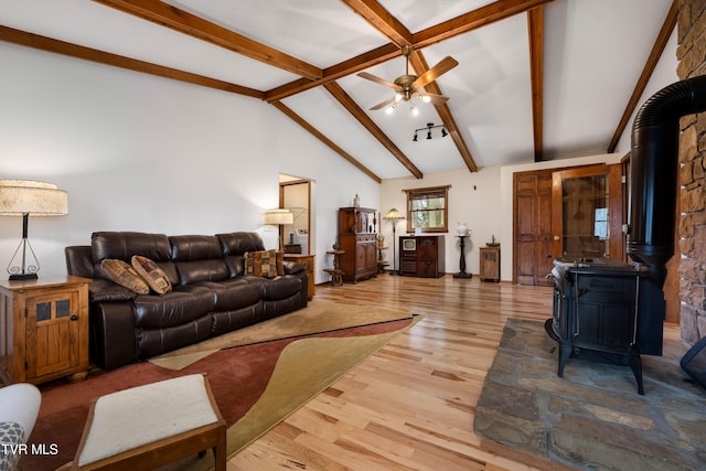 living room featuring a wood stove, light wood-style floors, beamed ceiling, ceiling fan, and high vaulted ceiling
