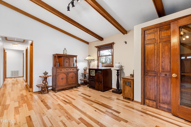 office space featuring baseboards, light wood-style flooring, attic access, visible vents, and vaulted ceiling with beams