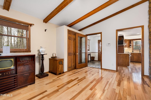 living area with light wood-style floors, french doors, lofted ceiling with beams, and baseboards