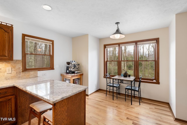 kitchen with a kitchen bar, a textured ceiling, light wood finished floors, baseboards, and backsplash