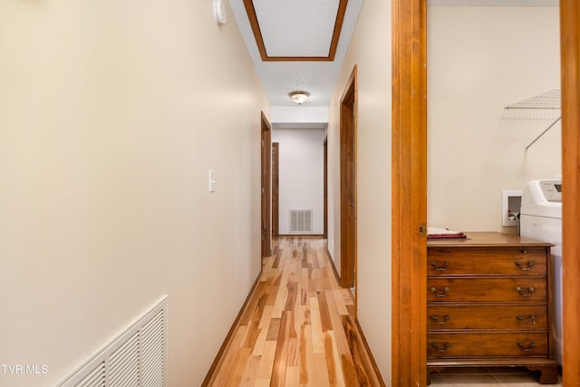 corridor with light wood finished floors, baseboards, visible vents, and washer / dryer