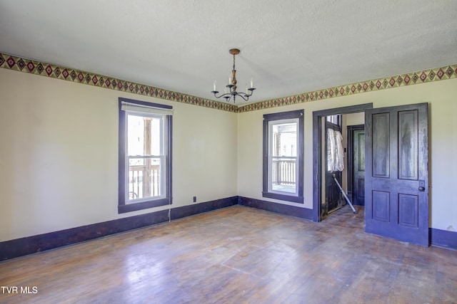 empty room featuring a textured ceiling, wood finished floors, an inviting chandelier, and baseboards